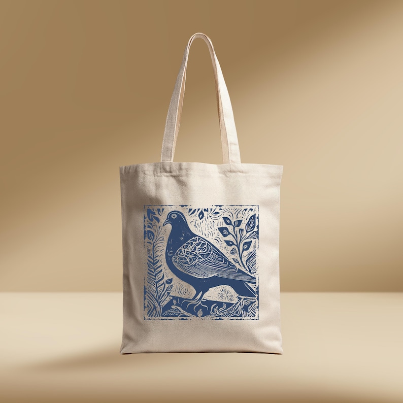 May include: A natural-coloured tote bag with a blue print of a pigeon and foliage. The design is a linocut style. The bag has long handles and a rectangular shape, suitable for carrying items.