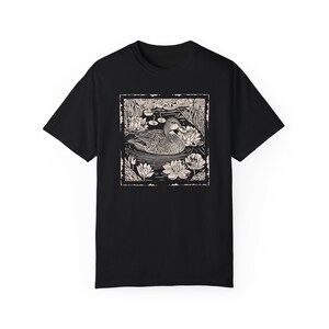 May include: Black t-shirt with a white graphic print of a duck swimming in a pond with lily pads.