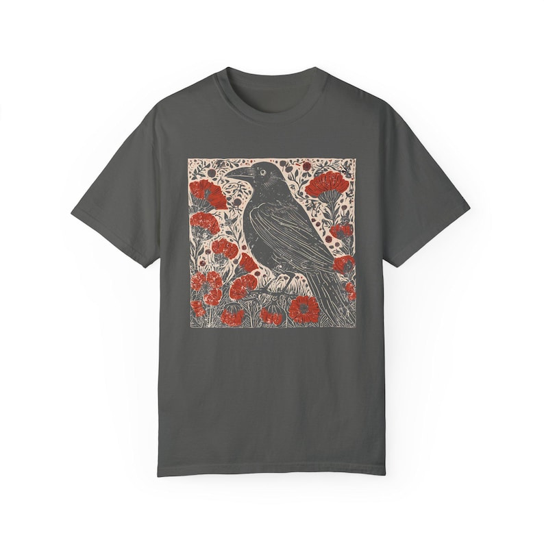 May include: A dark gray t-shirt with a black crow illustration surrounded by red flowers. The crow is perched on a branch with its wings spread out.