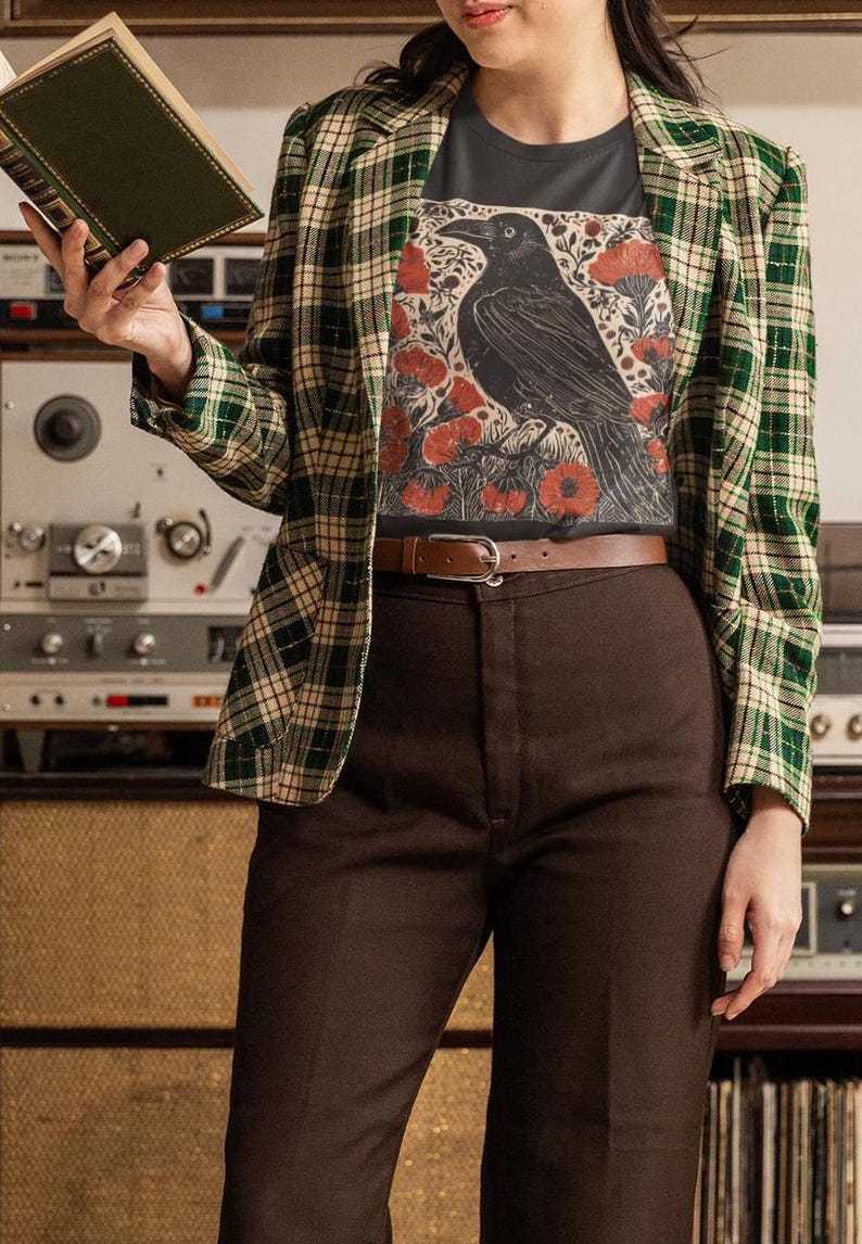 May include: A person wearing a black t-shirt with a graphic print of a black raven and red flowers. The t-shirt is worn under a green and white plaid blazer. The person is wearing brown pants and a brown belt.