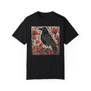 May include: Black t-shirt with a graphic print of a black crow standing in a field of red flowers.