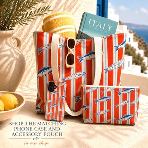 May include: A beach-themed set featuring a tote bag, phone case, and accessory pouch, all with a red and white striped pattern and fish illustrations. The tote bag holds a yellow towel, sunglasses, and a book titled "ITALY".
