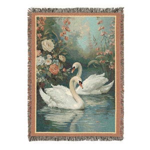 Puede incluir: Manta tejida que presenta una escena serena de dos cisnes blancos en un lago, rodeados de flores. La manta tiene un borde con flecos y una paleta de colores de azules, verdes y rosas suaves, creando una est&eacute;tica vintage.