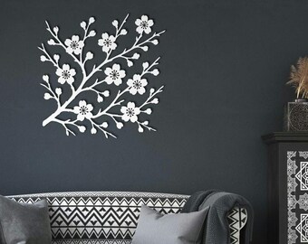 May include: White floral branch wall decor. The wall art features a square design with a branch of flowers. The flowers have detailed petals and a dark center. The wall decor is mounted on a dark gray wall.