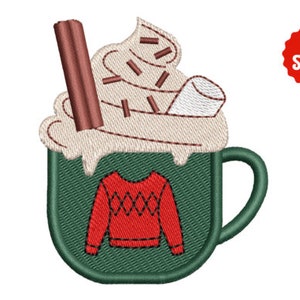 Può includere: Design ricamato di una tazza verde piena di panna montata, scaglie di cioccolato, un bastoncino di cannella e un marshmallow. La tazza presenta un motivo a maglione rosso. Un cerchio rosso con la scritta "3 dimensioni" è nell'angolo in alto a destra.