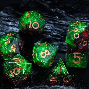 May include: A set of seven polyhedral dice in various shapes. The dice are a translucent green with copper-coloured numbers and glitter. Some dice have a red gradient. The dice are for tabletop games.