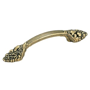May include: An antique brass-toned metal cabinet pull handle featuring a curved, ribbed center section and decorative ends molded with detailed, raised fruit and leaf motifs. The hardware has a weathered, textured finish throughout its surface.