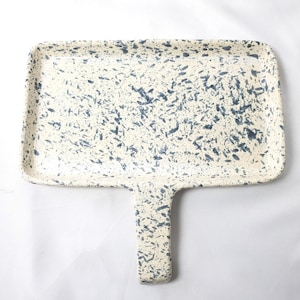 May include: A rectangular ceramic serving tray with a handle, featuring a cream-colored base with a speckled pattern of dark blue and gray flecks across the entire surface, including the handle and the raised edges of the tray.