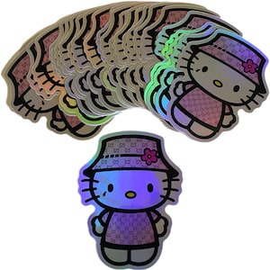 May include: A stack of holographic stickers featuring a cartoon cat wearing a pink bucket hat with a flower. The cat is wearing a pink and white patterned outfit with the letters "GG" repeated throughout.