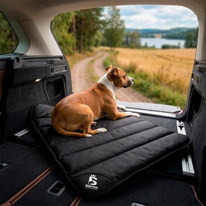 Puede incluir: Un perro marrón y blanco sentado sobre una alfombrilla rectangular negra acolchada para mascotas con costuras horizontales. La alfombrilla presenta un logotipo blanco en la esquina con el texto BOSYAK PREMIUM FOR PETS. Está colocada en el maletero de un vehículo.