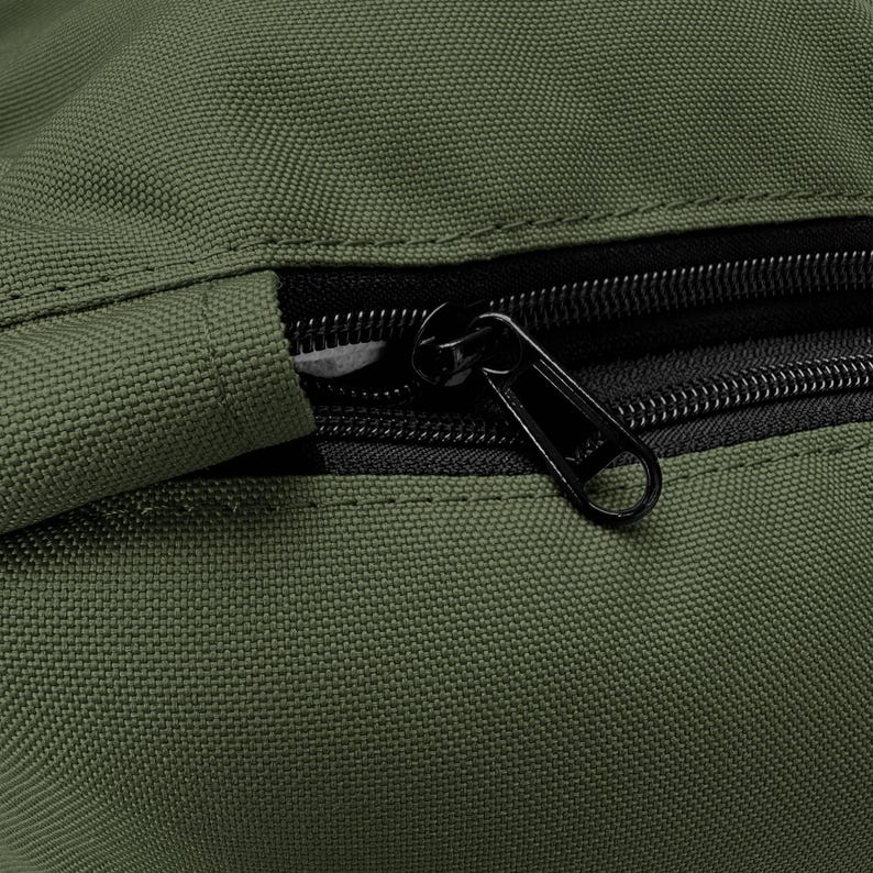 May include: Close-up of a section of a green canvas bag with a black zipper. The zipper is partially open, revealing the black interior. The bag's fabric has a textured appearance.