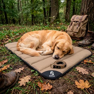 Puede incluir: Una alfombrilla rectangular de color tostado para mascotas con borde negro y un parche negro en la esquina que muestra el logotipo y el texto blanco BOSYAK. Una correa enrollada de color tostado y negro con una hebilla metálica dorada descansa.