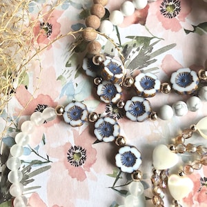 May include: Three beaded bracelets with different styles and colours. The first bracelet is made of white beads, the second is made of brown wooden beads, and the third is made of white and blue floral beads.