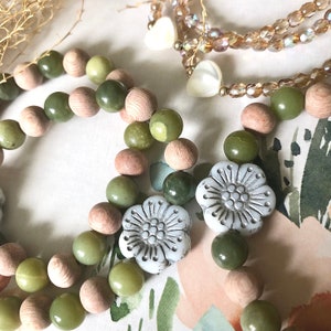 May include: Two green and brown beaded bracelets with white flower charms. The bracelets are made of natural stones and wood.