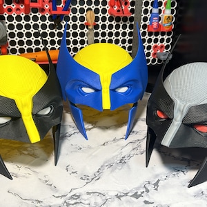 May include: Three 3D printed Wolverine masks, one with a yellow and black colour scheme, one with a blue and black colour scheme, and one with a grey and black colour scheme.