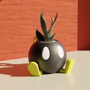 May include: A black, round planter shaped like a cartoon bomb, with white eyes and a white oval on each side. The planter has green feet and holds a green plant with long, slender leaves. The background is a textured orange wall.