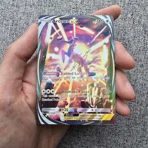 May include: A Pokemon trading card featuring Arceus ex, a legendary Pokemon with a golden and purple design. The card has a HP of 140 and an ability called "Fabled Luster". The card also has an attack called "Ultimate Force" that does 70+ damage.