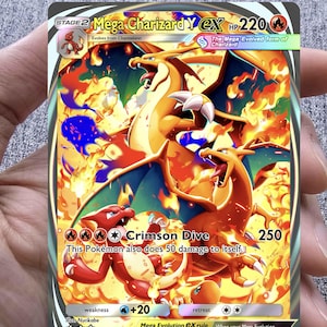 May include: A Mega Charizard Y EX Pokémon trading card. The card features a fiery orange and yellow Charizard with blue accents, flames, and the text "Crimson Dive". The card has a HP of 220 and a retreat cost of two stars.