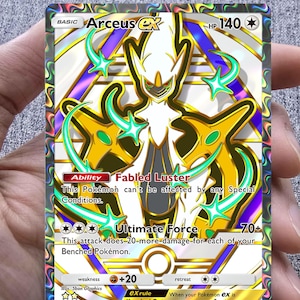 May include: A holographic Arceus ex Pokémon trading card. The card features a gold, white, and teal design with the text "Arceus ex" and "Ultimate Force". The card has a HP of 140 and the text "Fabled Luster".