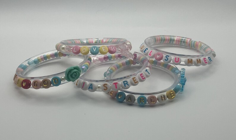 May include: Five clear plastic bangles with colourful beads spelling out words such as "LOVE", "WELCOME SUMMER", and "LIA STREET". Some bangles have decorative accents like a rose or a butterfly.