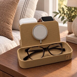 Op de afbeelding: Een beige, geribbeld oplaadstation met een ronde magnetische lader, een bakje voor accessoires en een klein vierkant embleem met de letter F. Het station bevat een witte oortjes-case en een smartwatch met een bruine leren band.