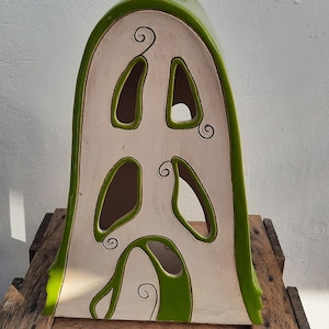 Könnte beinhalten: Ein weißes Keramikhaus in Form eines abgerundeten Bogens mit grünem Besatz und ausgeschnittenen Fenstern. Das Haus hat ein verspieltes Design mit grünen Spiralen, die auf die Vorderseite gemalt sind.