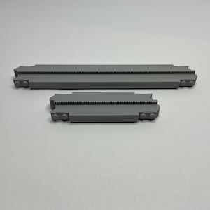 May include: Two gray plastic track pieces for a toy train set. The larger piece is about 10 inches long and the smaller piece is about 5 inches long.