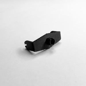 Könnte beinhalten: Ein schwarzes, 3D-gedrucktes Kunststoffobjekt mit einer einzigartigen Form, das einen gebogenen Abschnitt und eine zylindrische Öffnung aufweist. Das Objekt scheint ein kleines, funktionelles Bauteil zu sein, möglicherweise für ein größeres Gerät oder System. Das Design ist schlicht und modern.