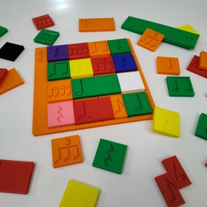 May include: A colorful musical puzzle with orange, green, yellow, red, purple, pink, and white tiles. Each tile has a different musical symbol, such as a treble clef, a note, or a set of five lines. The puzzle is laid out on a white surface.