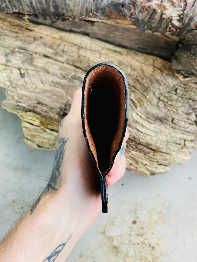 May include: A black leather wallet with a brown interior. The wallet is held open, revealing the inside. The edges are neatly stitched, and the leather has a slightly textured appearance. The wallet is designed to hold cards and cash.