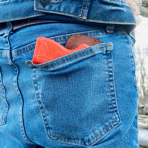 K&ouml;nnte beinhalten: Eine rote Pistole steckt in der Ges&auml;&szlig;tasche einer blauen Jeans.