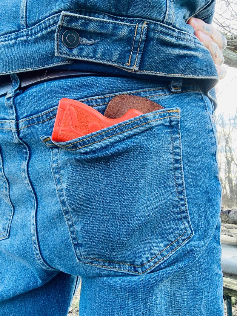 K&ouml;nnte beinhalten: Eine rote Pistole steckt in der Ges&auml;&szlig;tasche einer blauen Jeans.