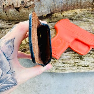 K&ouml;nnte beinhalten: Ein braunes Lederholster mit schwarzen N&auml;hten. Das Holster ist offen und leer.
