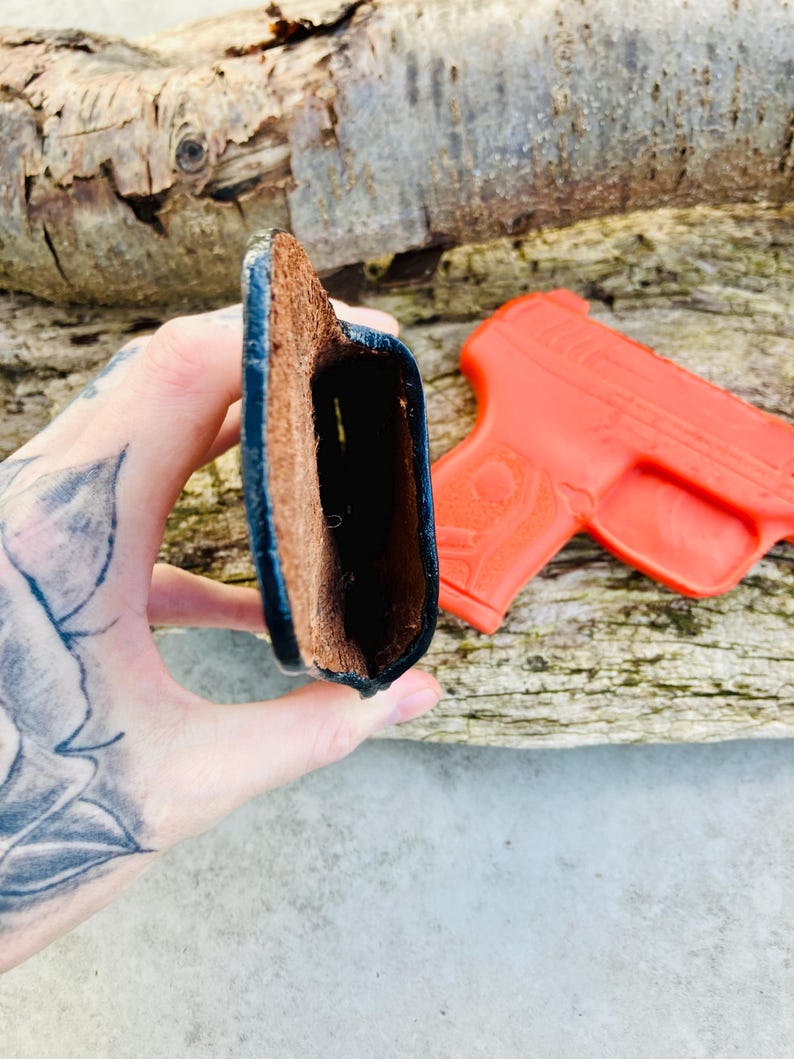 K&ouml;nnte beinhalten: Ein braunes Lederholster mit schwarzen N&auml;hten. Das Holster ist offen und leer.