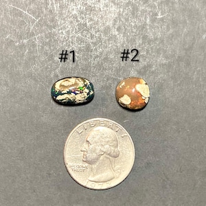 Puede incluir: Dos piedras preciosas ovaladas, etiquetadas #1 y #2, junto a una moneda de veinticinco centavos. La piedra preciosa #1 es ovalada con una mezcla de colores. La piedra preciosa #2 es redonda con tonos naranja y marrón. La moneda es de 1972.