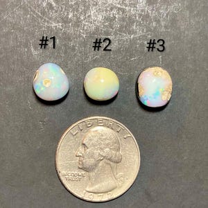 Puede incluir: Tres piedras preciosas de ópalo con colores iridiscentes se muestran junto a un cuarto de dólar estadounidense. Las piedras preciosas están numeradas #1, #2 y #3. La moneda muestra el perfil de George Washington y el año 1972.