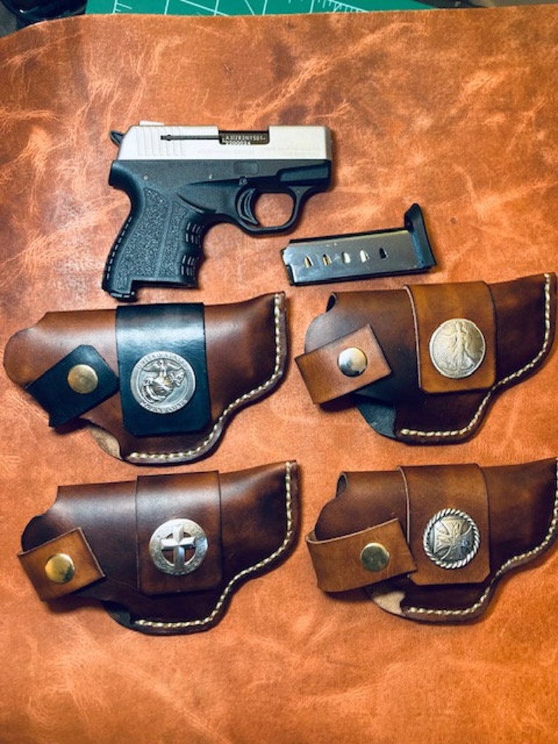Op de afbeelding: Vier bruine leren holster met zilveren accenten en decoratieve ontwerpen. De holster zijn ontworpen om een klein, zilveren pistool te dragen.