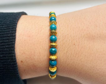 May include: A blue and gold beaded bracelet with a decorative design. The bracelet is made of small, round beads with a gold finish.