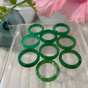 May include: Eight green jade rings of varying sizes, displayed on a white surface.