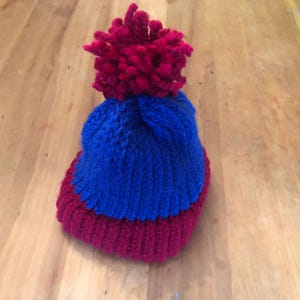 May include: A blue and burgundy knitted hat with a large burgundy pom-pom on top.