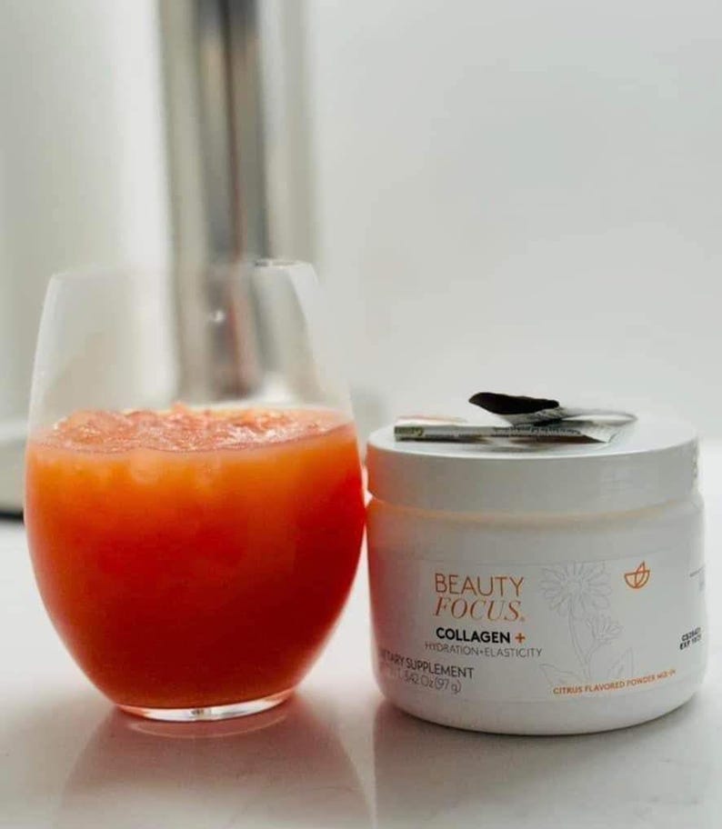 Puede incluir: Un tarro blanco de suplemento diet&eacute;tico en polvo de col&aacute;geno Beauty Focus+ con sabor a c&iacute;tricos. El tarro est&aacute; sobre una superficie blanca junto a un vaso de zumo de naranja.