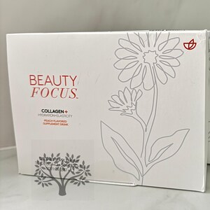 Puede incluir: Caja blanca con un dise&ntilde;o de flor estilizado y el texto "BEAUTY FOCUS" en rojo y negro. La caja tambi&eacute;n tiene el texto "COLLAGEN + HYDRATION + ELASTICITY" y "PEACH FLAVORED SUPPLEMENT DRINK" en negro.