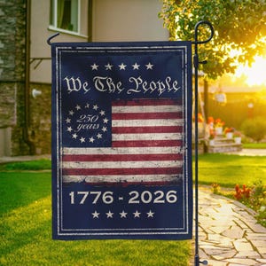 May include: A rectangular garden flag with a distressed American flag design. The flag has the text "We The People" and "1776-2026". It has a navy blue border and is mounted on a black pole. The flag is displayed outdoors.