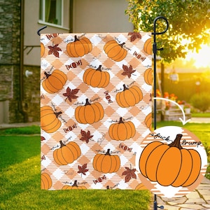 May include: A garden flag with a repeating pattern of orange pumpkins, brown leaves, and candy on a white and orange checkered background. The flag also has the words "fuck trumps" on the pumpkins.