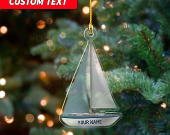 May include: Clear acrylic sailboat Christmas ornament with a gold hanging string. The boat features a white sail and blue trim. The text "YOUR NAME" is printed on the boat. The text "CUSTOM TEXT" is printed on a red rectangle.