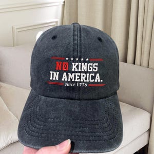 May include: A black baseball cap with the text "NO KINGS IN AMERICA. since 1776" embroidered in white and red.