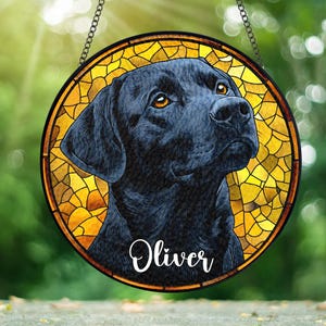 May include: A stained glass window hanging with a black Labrador Retriever portrait. The dog is looking up with its mouth closed. The background is a yellow and orange stained glass design. The dog's name, "Oliver", is written in white cursive lettering below the dog's head.