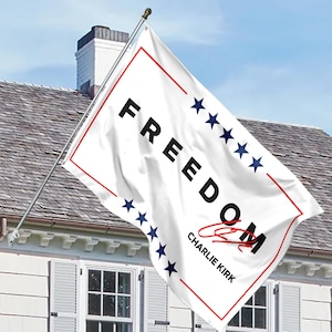 May include: White flag with the word "FREEDOM" in black block letters, a red border, and blue stars. The flag also features the name "Charlie Kirk" in black and red script.
