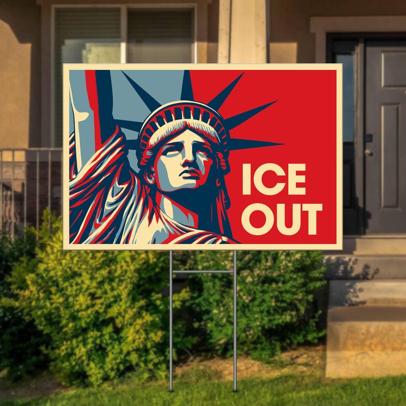 May include: A yard sign featuring a stylized image of the Statue of Liberty in red, white, and blue. The words "ICE OUT" are printed in bold white letters on a red background. The sign is displayed on a metal frame in a grassy yard.