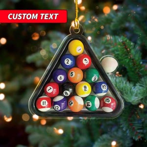 May include: A clear, triangular ornament holding a set of billiard balls. The balls are numbered and colored, arranged in a triangle. The ornament has a gold string for hanging, and the top has a red rectangle with the text "CUSTOM TEXT".